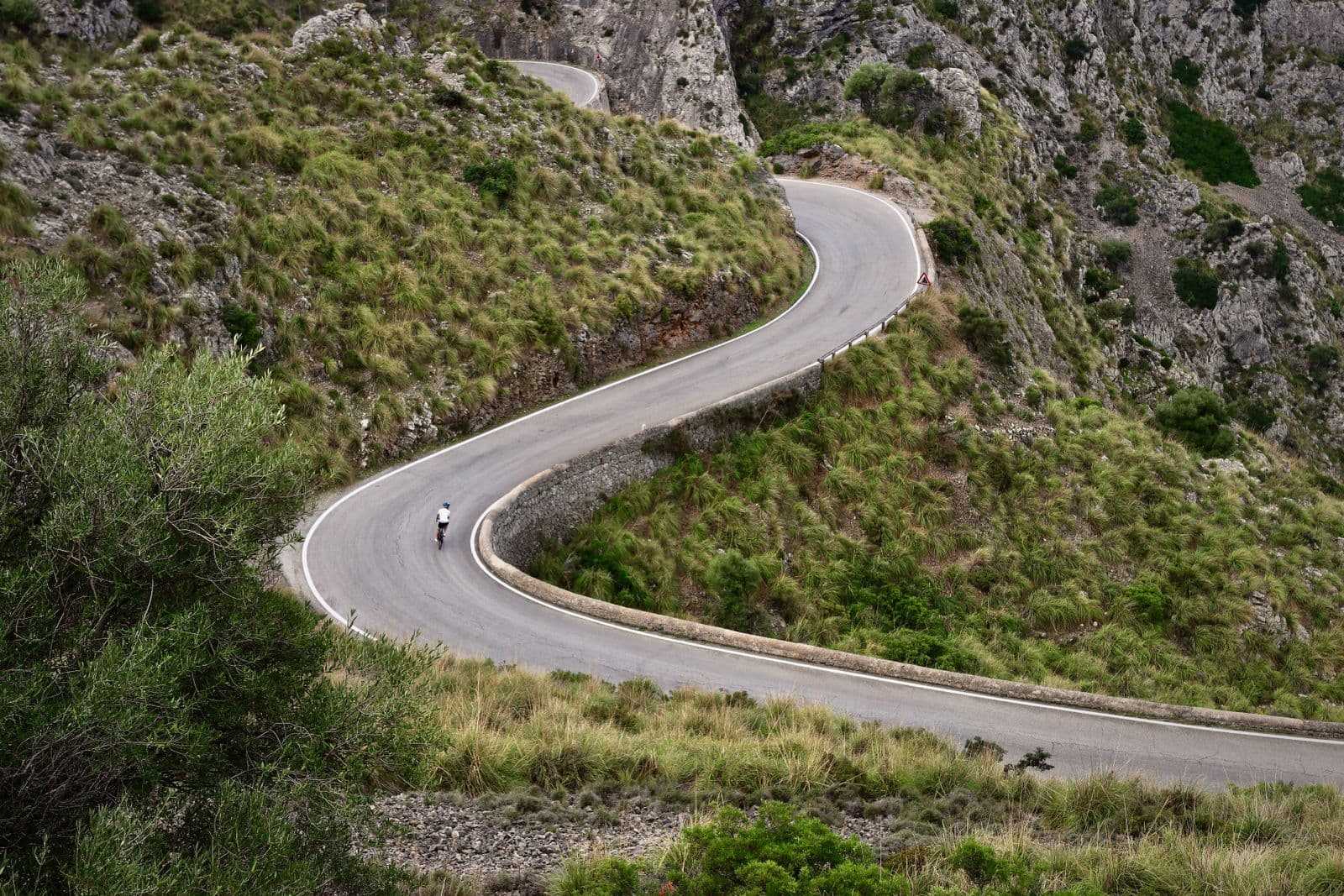 A cyclist descending a winding S-curve mountain road