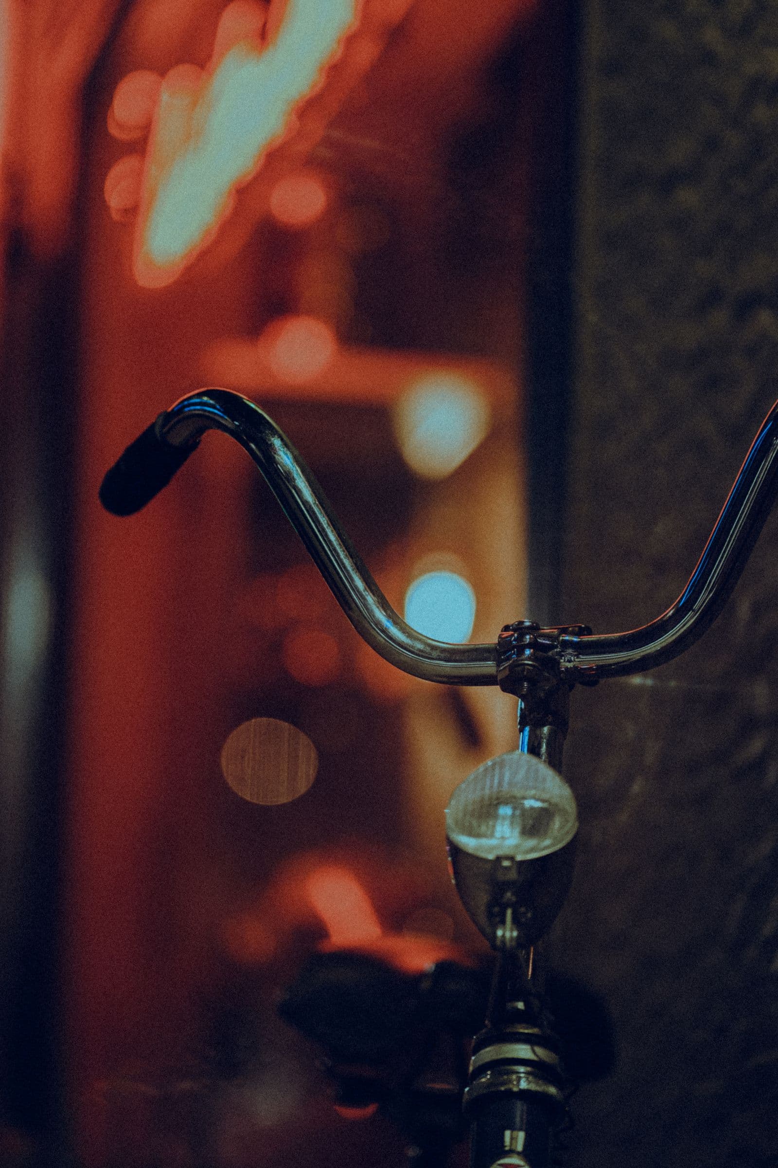 Chrome handlebars and a vintage headlamp silhouetted against warm neon light