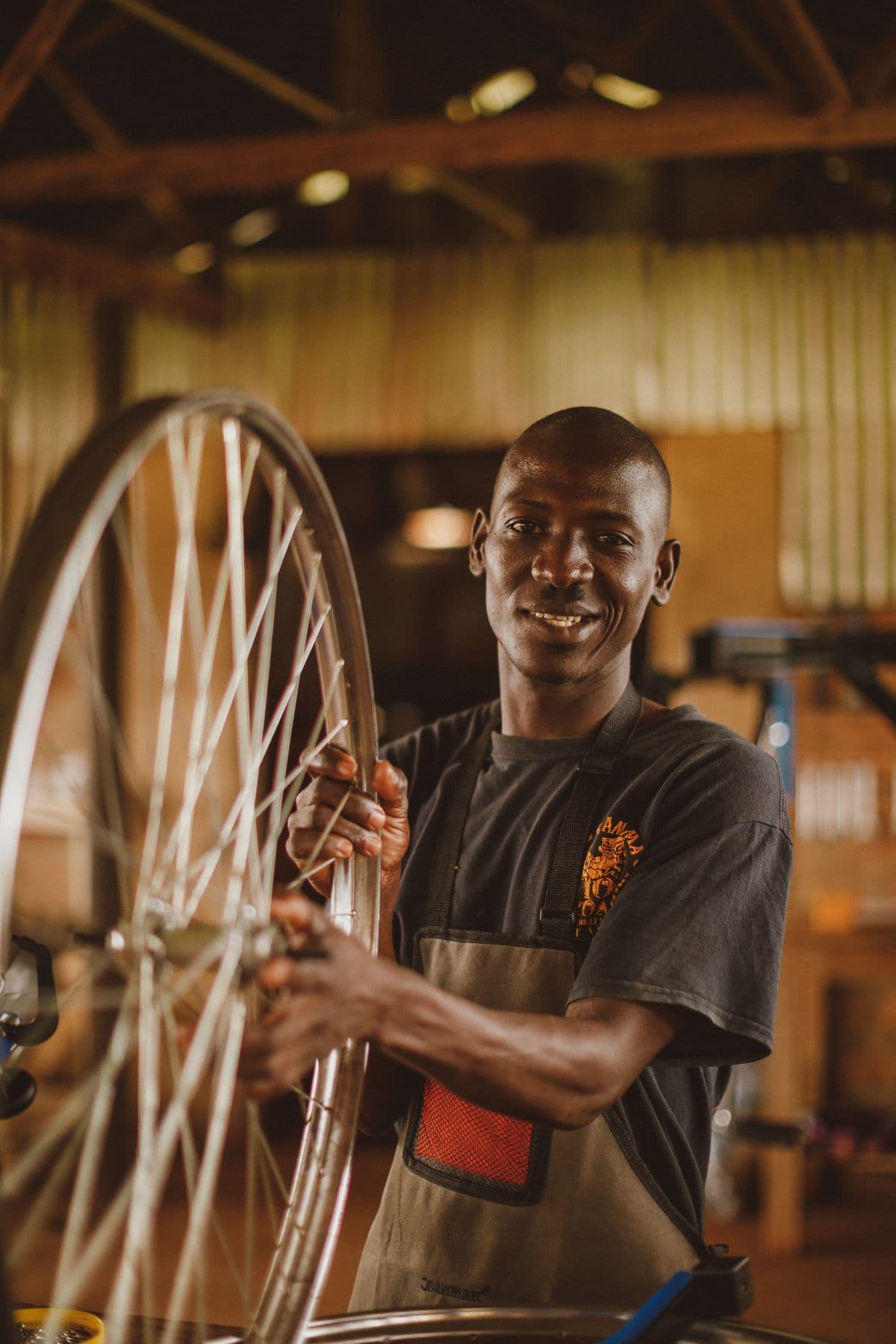 A smiling mechanic holding a freshly built wheel in a warm workshop