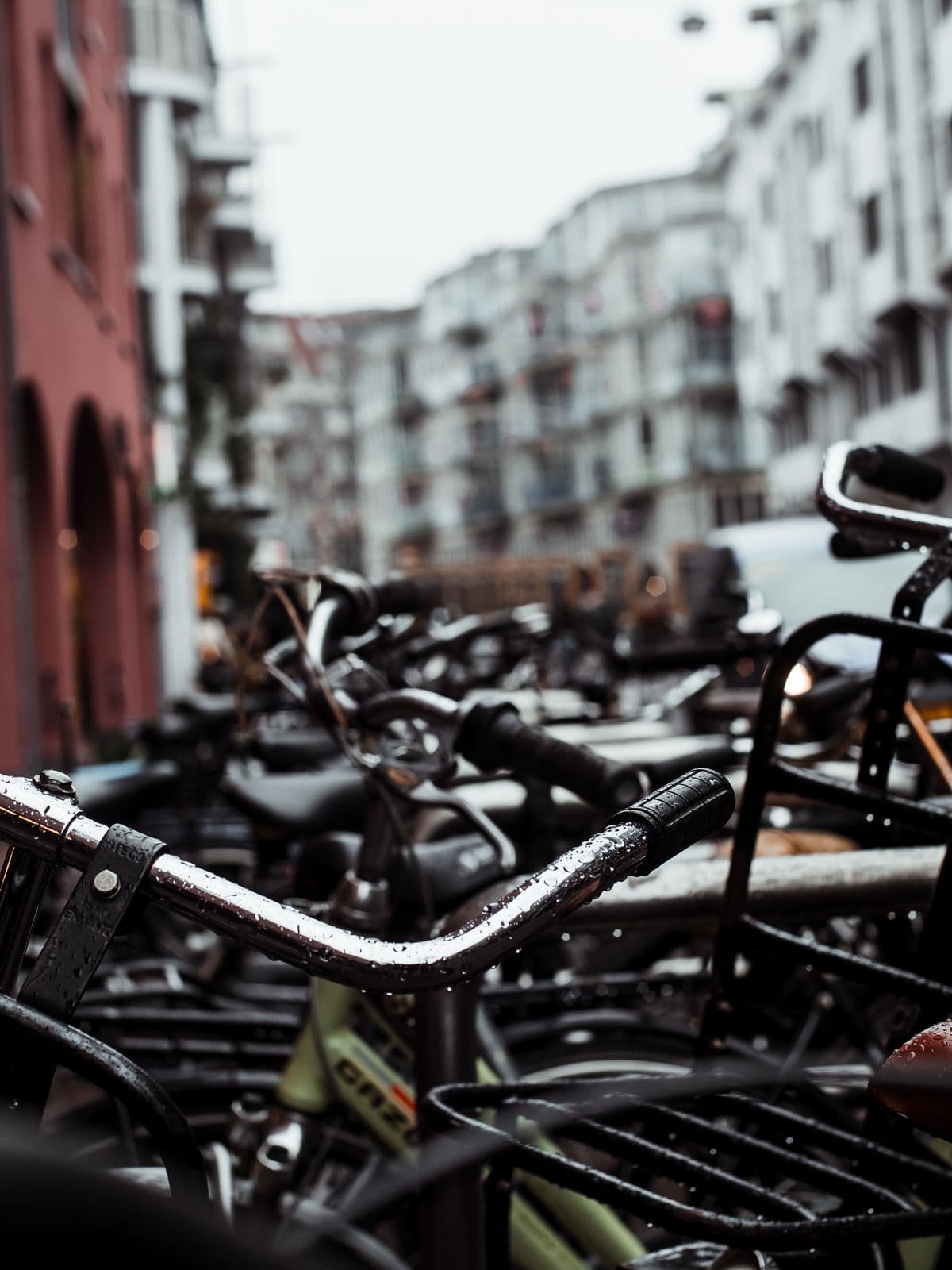 Rain-beaded chrome handlebars of parked bikes on a moody city street