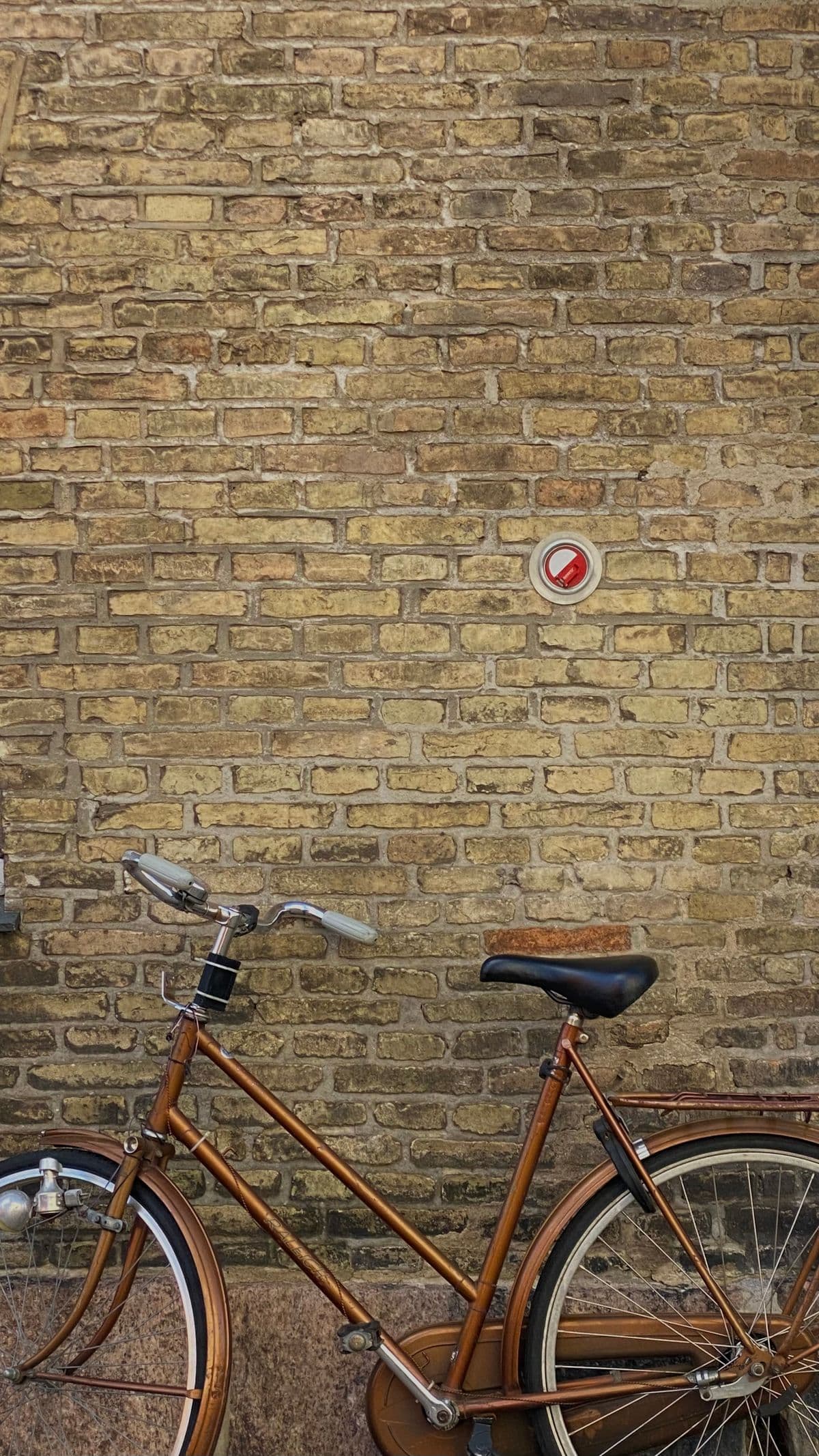 A restored copper-bronze vintage Raleigh bicycle against a yellow brick wall