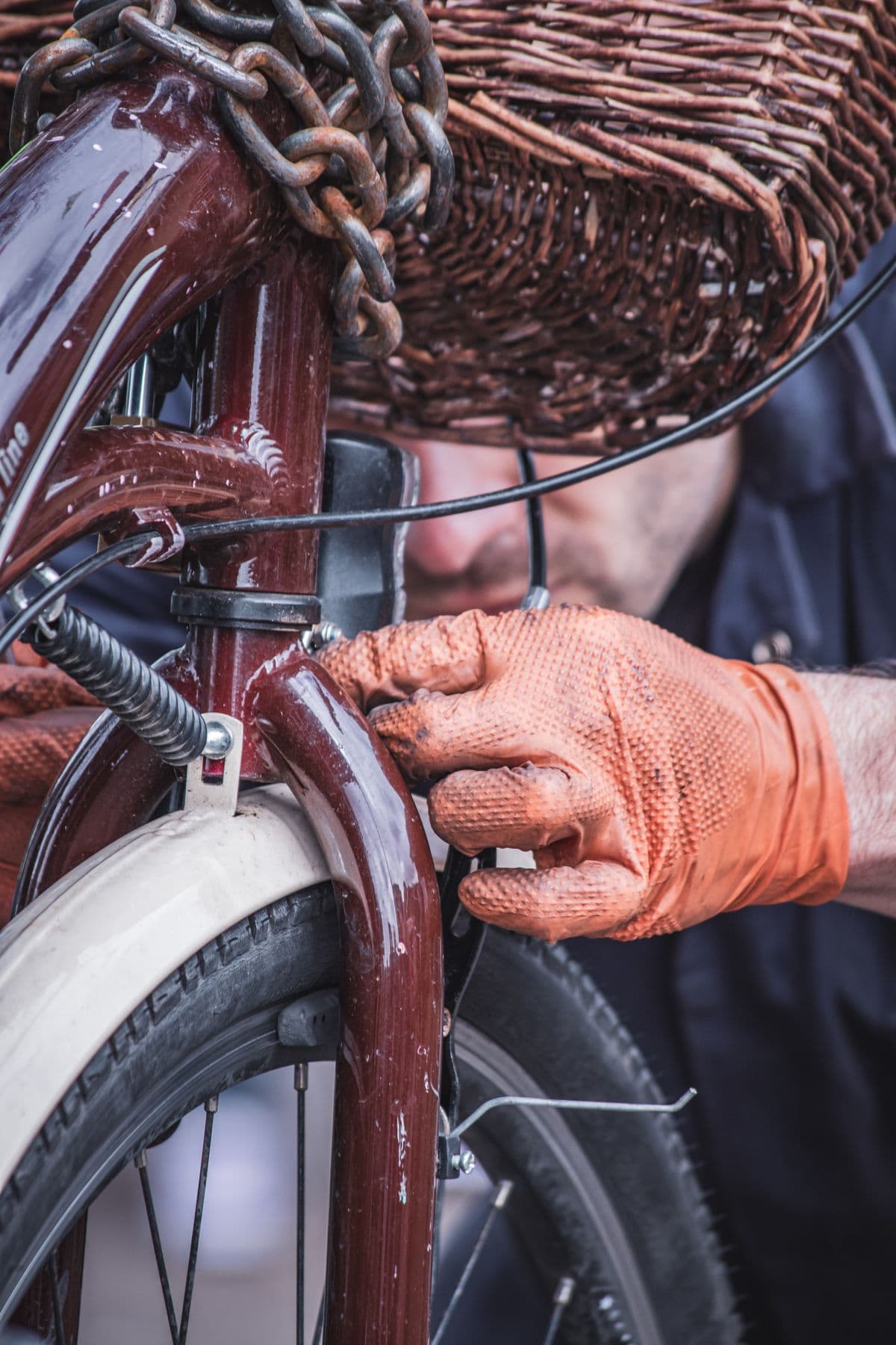 Orange-gloved hands servicing the fork of a glossy burgundy vintage bicycle
