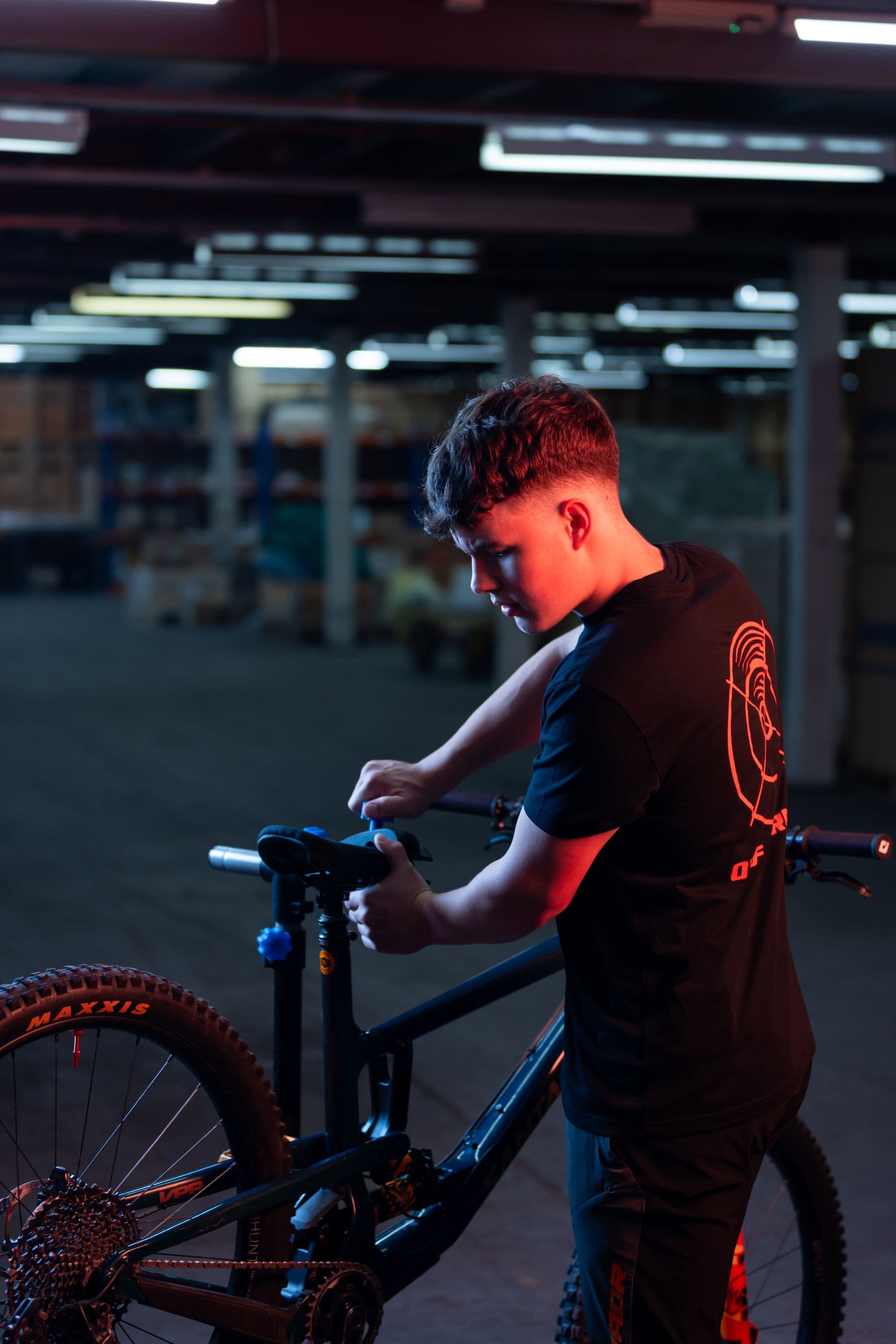 A mechanic working on a mountain bike in a dark workshop with red rim lighting